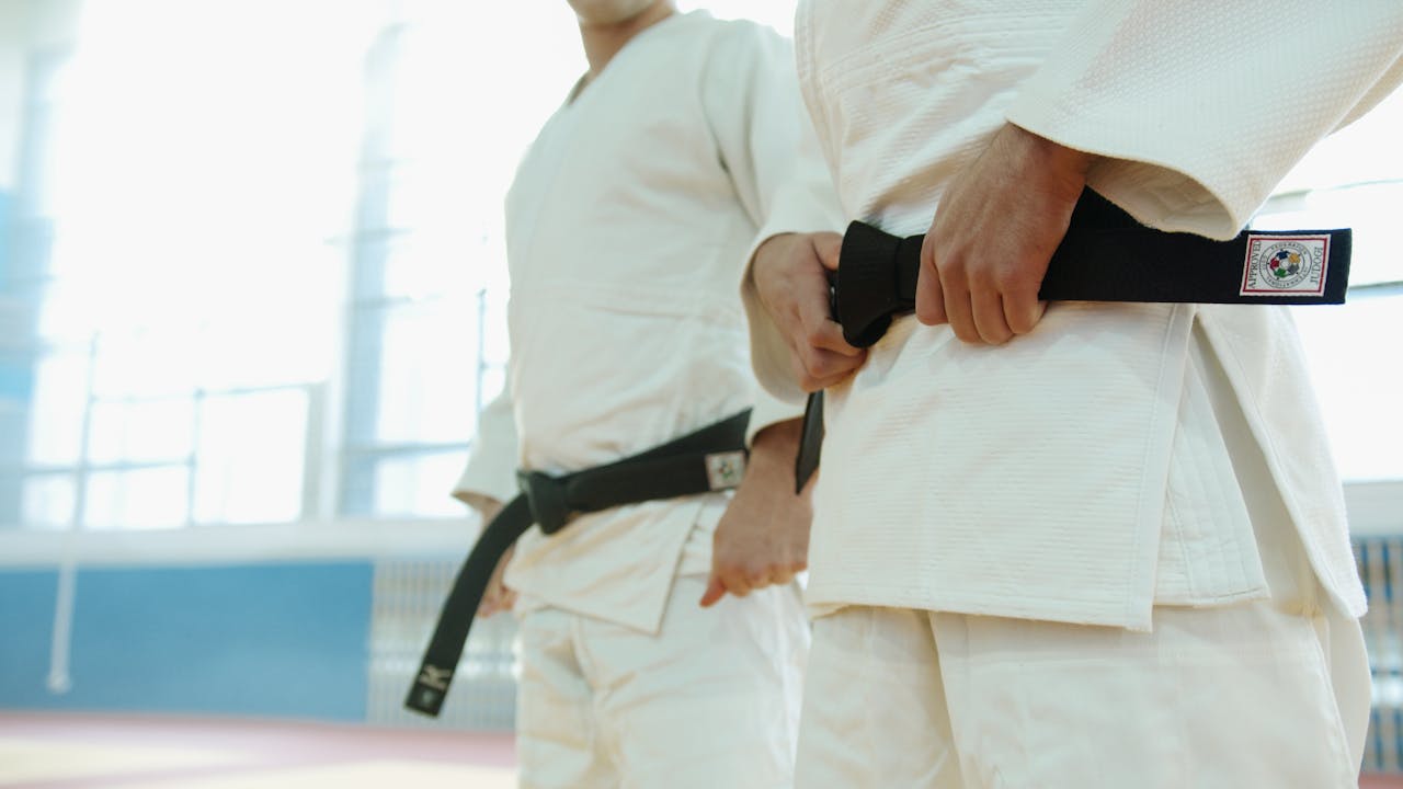 Two martial artists in white uniforms holding black belts, showcasing discipline and strength.