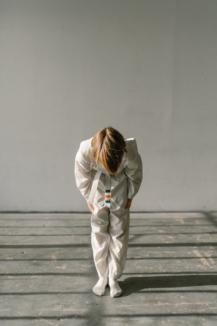 A child bows in a martial arts gi, practicing respect and discipline indoors.